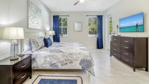 A bedroom with a bed, nightstands, a dresser, a ceiling fan, and a painting of a beach scene. - Peaceful Naples Gateway (Naples)