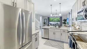 A modern kitchen with stainless steel appliances, light-colored cabinets, and pendant lighting. - Peaceful Naples Gateway (Naples)