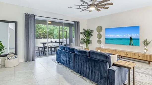 A modern living room with a blue sofa, a ceiling fan, a large TV, and a view of the outdoors. - Peaceful Naples Gateway (Naples)