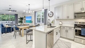 A modern kitchen with white cabinets, a central island, stainless steel appliances, and a dining area with a view of the outdoors. - Peaceful Naples Gateway (Naples)
