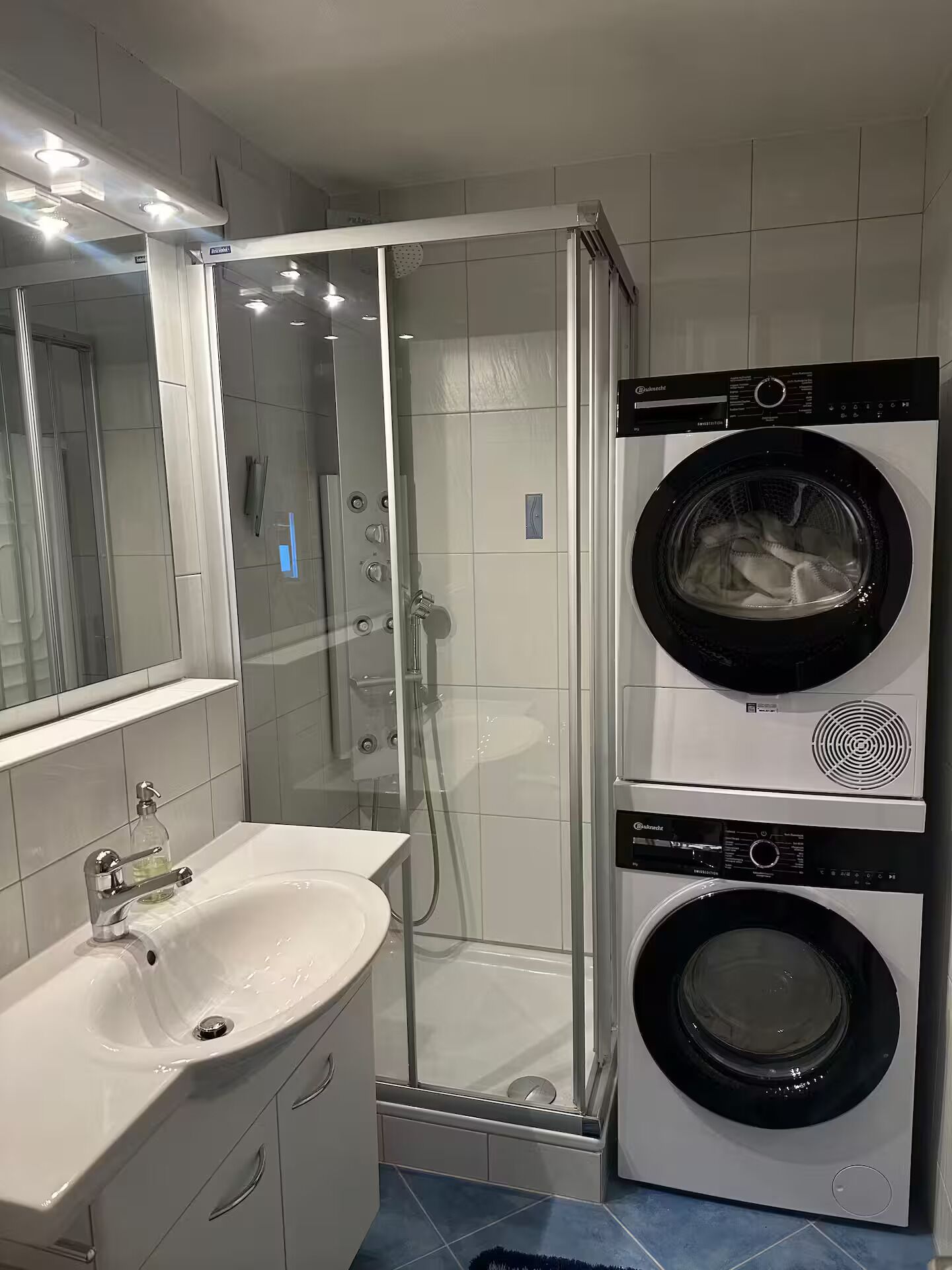 Une salle de bain moderne avec une douche à parois de verre, un lavabo et un lave-linge et un sèche-linge superposés.