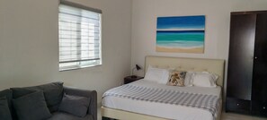 Ein Schlafzimmer mit einem Bett, einer Couch, einem Strandbild und einer Tür.