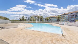 A swimming pool with a tiled deck, surrounded by a fence, and a building with multiple balconies in the background. - Seaside Apartment in Saint-Cyprien-Plage (66750), Lagune Area (Saint-Cyprien Plage)