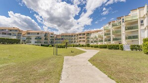 A residential building with multiple balconies, a grassy lawn, and a pathway leading to the entrance. - Seaside Apartment in Saint-Cyprien-Plage (66750), Lagune Area (Saint-Cyprien Plage)