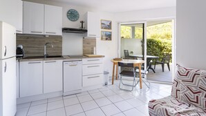 A compact kitchen with white cabinets, a dishwasher, and a wooden countertop. There is a dining area with a table and chairs, and a sofa with patterned cushions. - Seaside Apartment in Saint-Cyprien-Plage (66750), Lagune Area (Saint-Cyprien Plage)