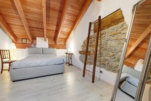 Ein Schlafzimmer mit Holzboden, Steinwand, Bett, einer Leiter und einem Spiegel.