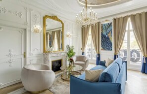 A luxurious living room with a white fireplace, a blue sofa, a round coffee table, and a large mirror with a gold frame. - AN UNIQUE STYLE COMBINES TIMELESS ARCHITECTURAL WITH MODERN AMENITIES – MARAIS (Paris)