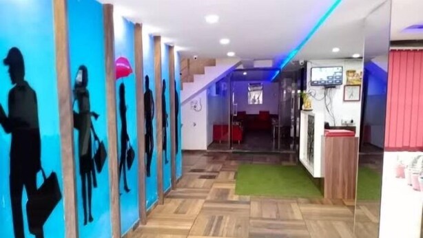 A hotel reception area with a wooden floor, a reception desk, and a staircase leading to an upper level. - Hotel Kuber (Rajkot)