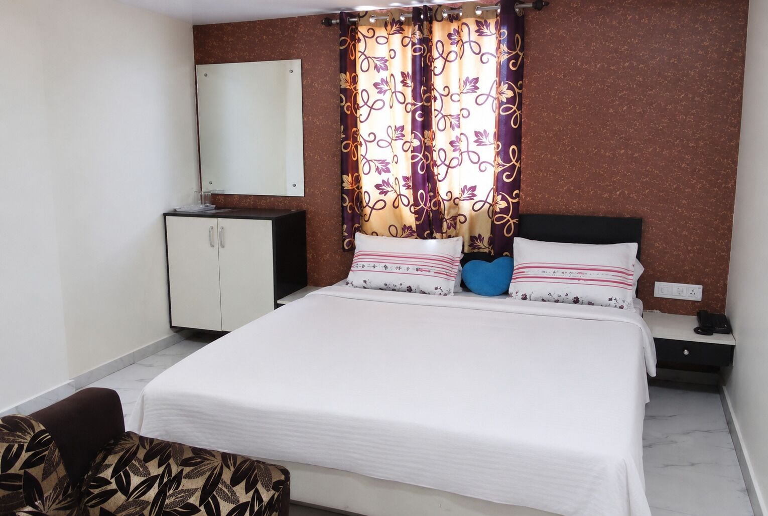 Une chambre d’hôtel avec un lit, une table de chevet, une armoire et un miroir au mur.