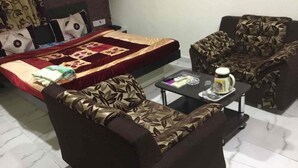 A hotel room with a bed, two sofas, a small table with a coffee pot, and a remote control. - Hotel Kuber (Rajkot)