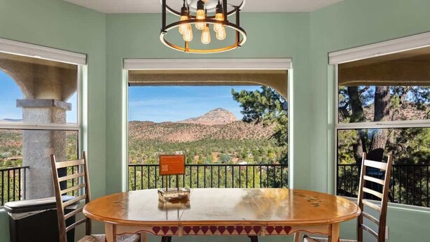 Un espace repas comprenant une table et des chaises, un lustre, et une vue sur un paysage montagneux grâce à de grandes fenêtres.
