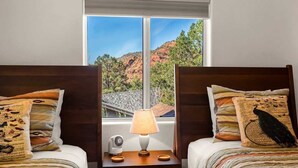 Une chambre avec deux lits, une table de chevet avec une lampe et une fenêtre donnant sur un paysage montagneux.