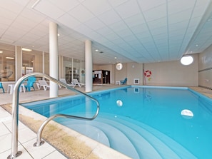 Ein Innenpool mit klarem Wasser, einer Metallleiter und Liegestühlen.