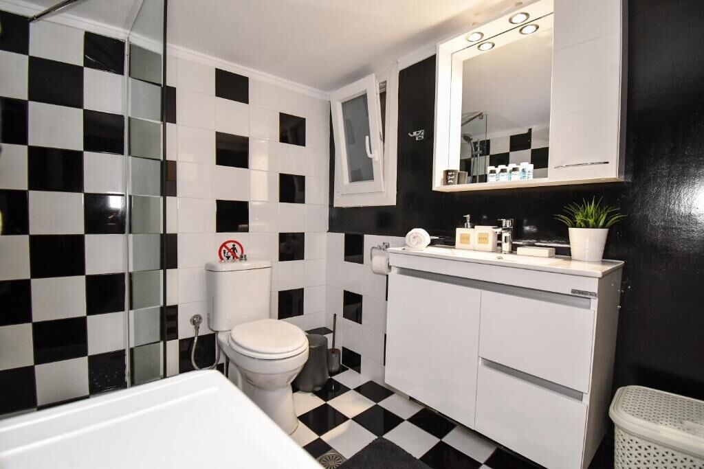 Une salle de bain avec un sol à carreaux noirs et blancs, des toilettes blanches, un lavabo blanc avec un miroir au-dessus et un meuble blanc en dessous.