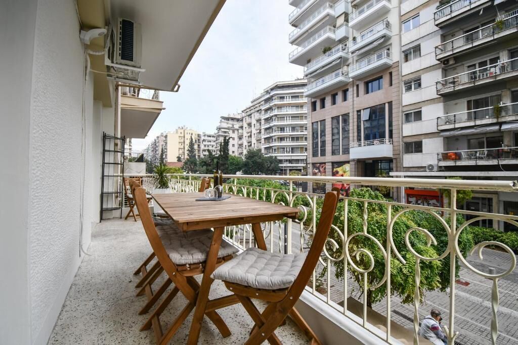 A balcony with a wooden table and chairs, overlooking a cityscape with multiple buildings.