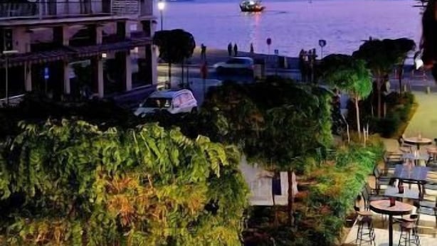 A view of a coastal area with a building, outdoor seating, and a body of water. - Porto Sea View Apartments - D. Gounari 5 (Thessaloniki)