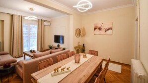 A modern living room with a wooden dining table, sofas, and a TV. - Porto Sea View Apartments - D. Gounari 5 (Thessaloniki)