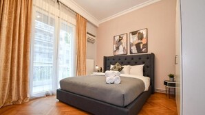 A bedroom with a large bed, a bedside table, a nightstand, and a window with curtains. - Porto Sea View Apartments - D. Gounari 5 (Thessaloniki)