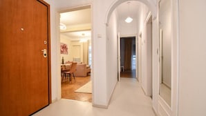 A hallway with a wooden door, white walls, and an archway leading to a living area with a sofa and a dining table. - Porto Sea View Apartments - D. Gounari 5 (Thessaloniki)