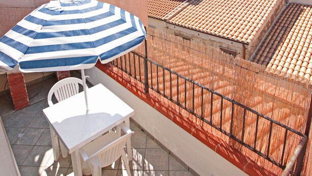A balcony with a striped umbrella, white table, and chairs, overlooking a mountainous landscape and terracotta-roofed buildings. - Terrazza Cathedral by Wonderful Italy (Cefalù)