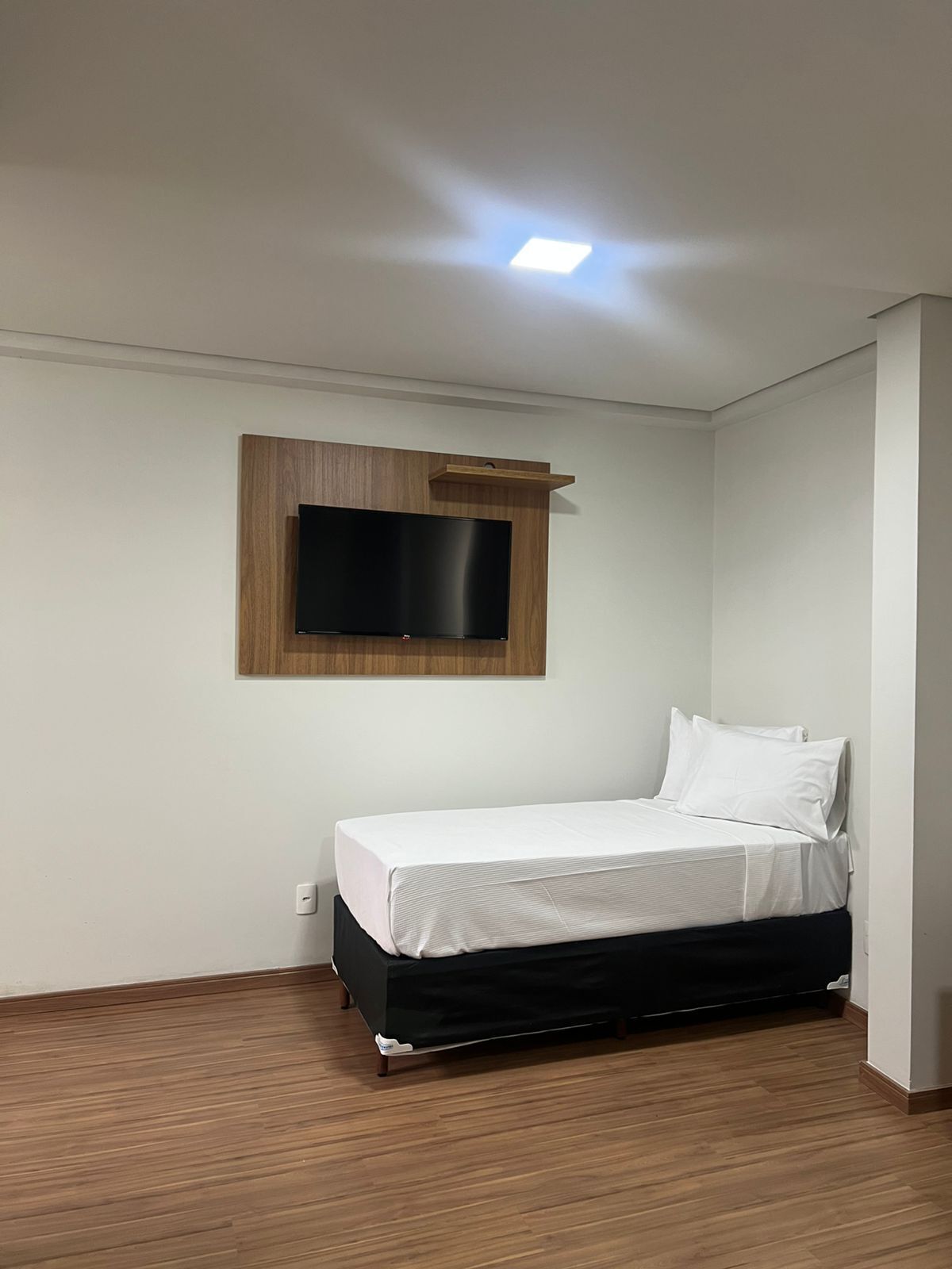 A small, neatly arranged bedroom with a single bed, a mounted TV, and a wooden floor.