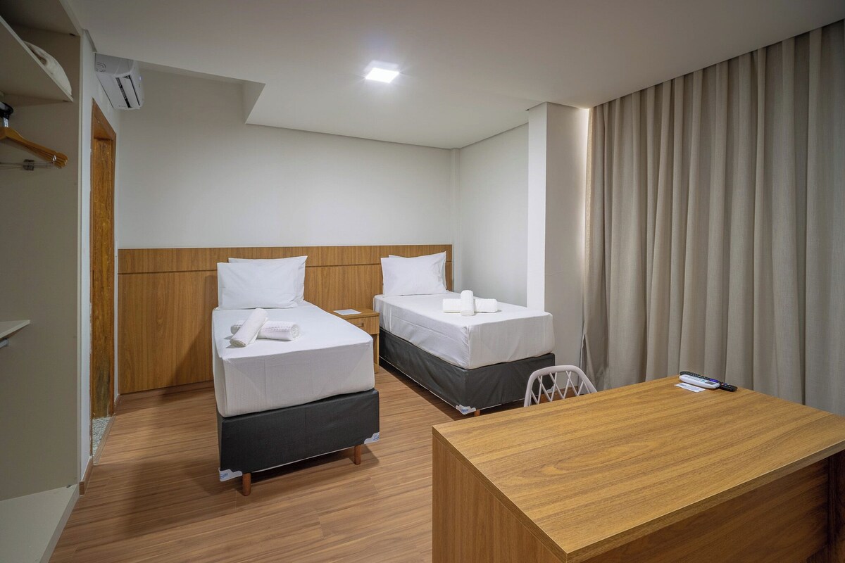 Une chambre d’hôtel avec deux lits, un bureau en bois et une fenêtre avec des rideaux.