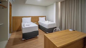 A hotel room with two beds, a wooden desk, and a window with curtains.