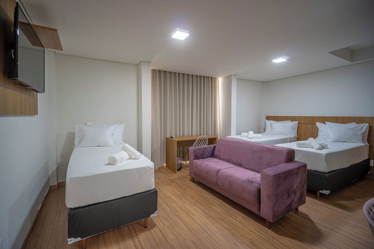 A hotel room with two single beds, a sofa, a TV mounted on the wall, and a wooden floor.
