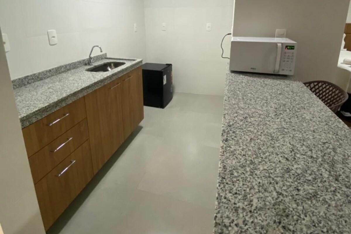A modern kitchen with granite countertops, wooden cabinets, a black trash bin, and a white microwave.