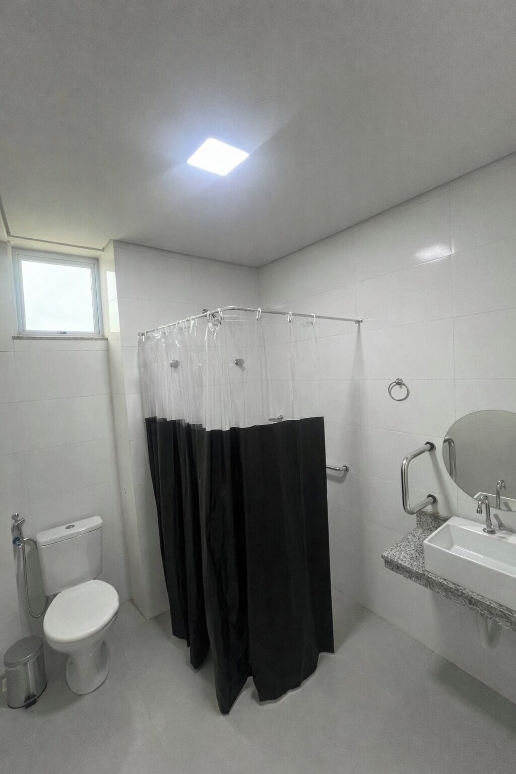 A bathroom with a shower curtain, toilet, sink, and a window.