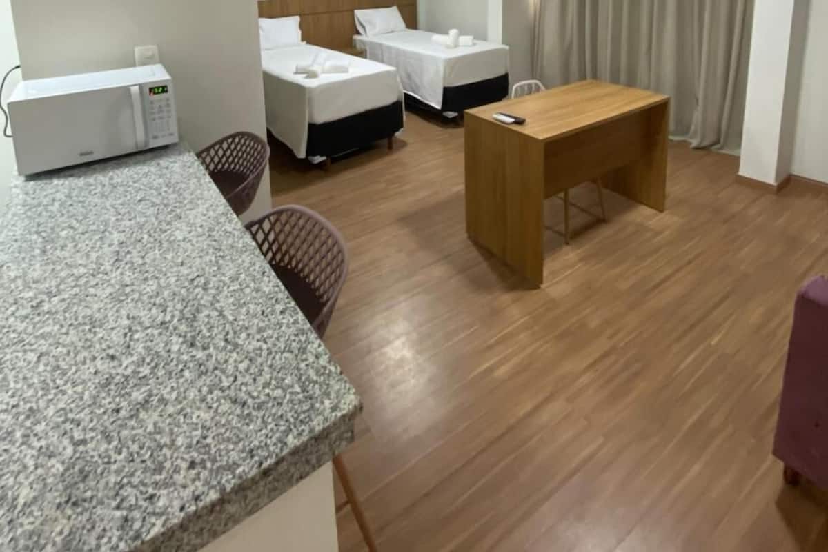 A hotel room with a kitchenette, two beds, a wooden desk, and a chair.