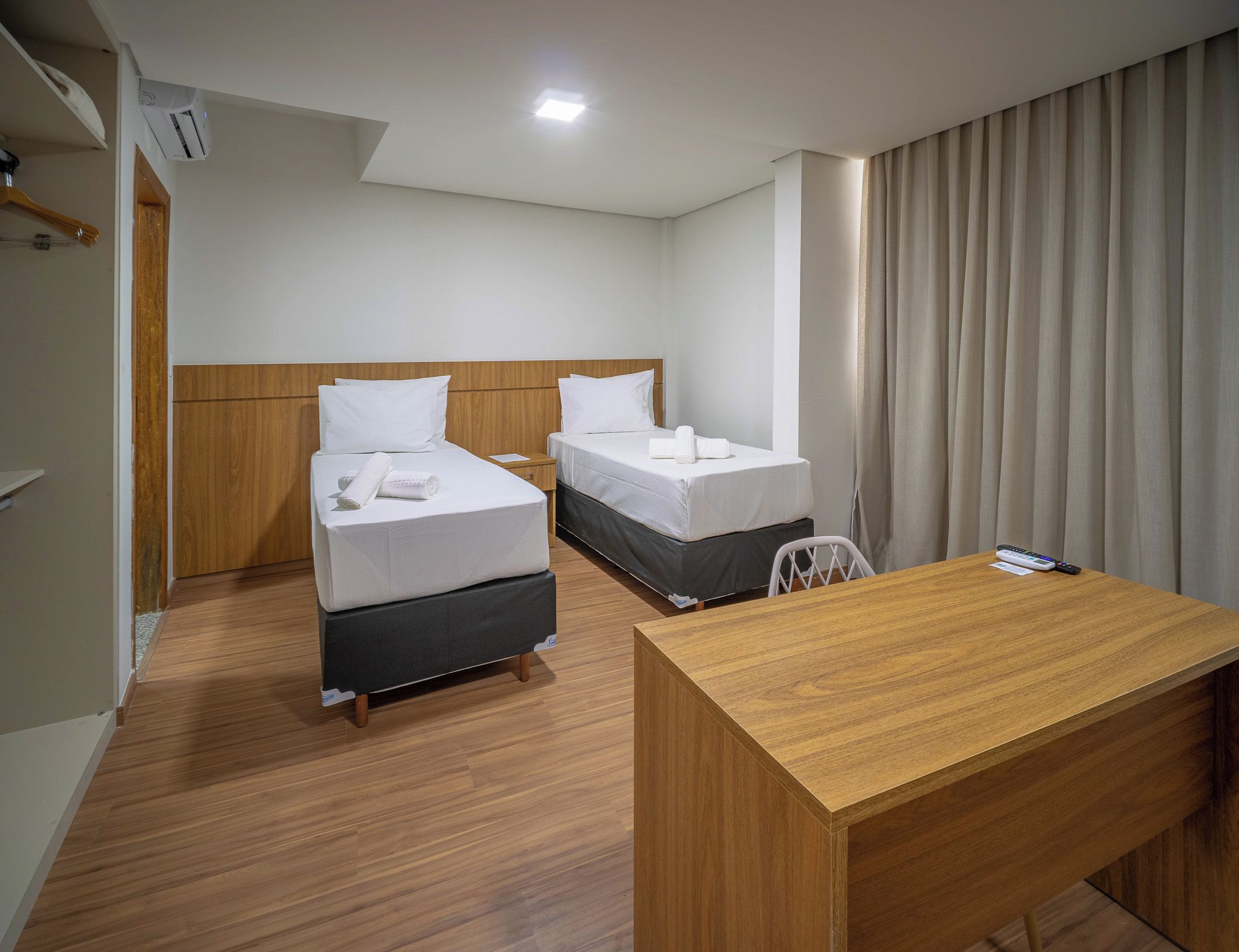 A hotel room with two beds, a wooden desk, and a window with curtains.
