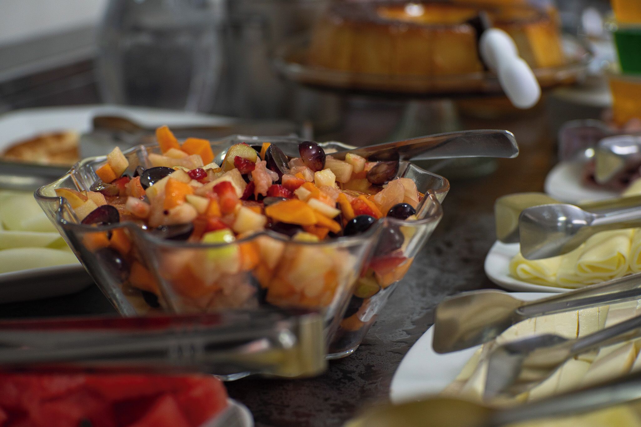 A buffet table with various dishes, including a fruit salad in a glass bowl.