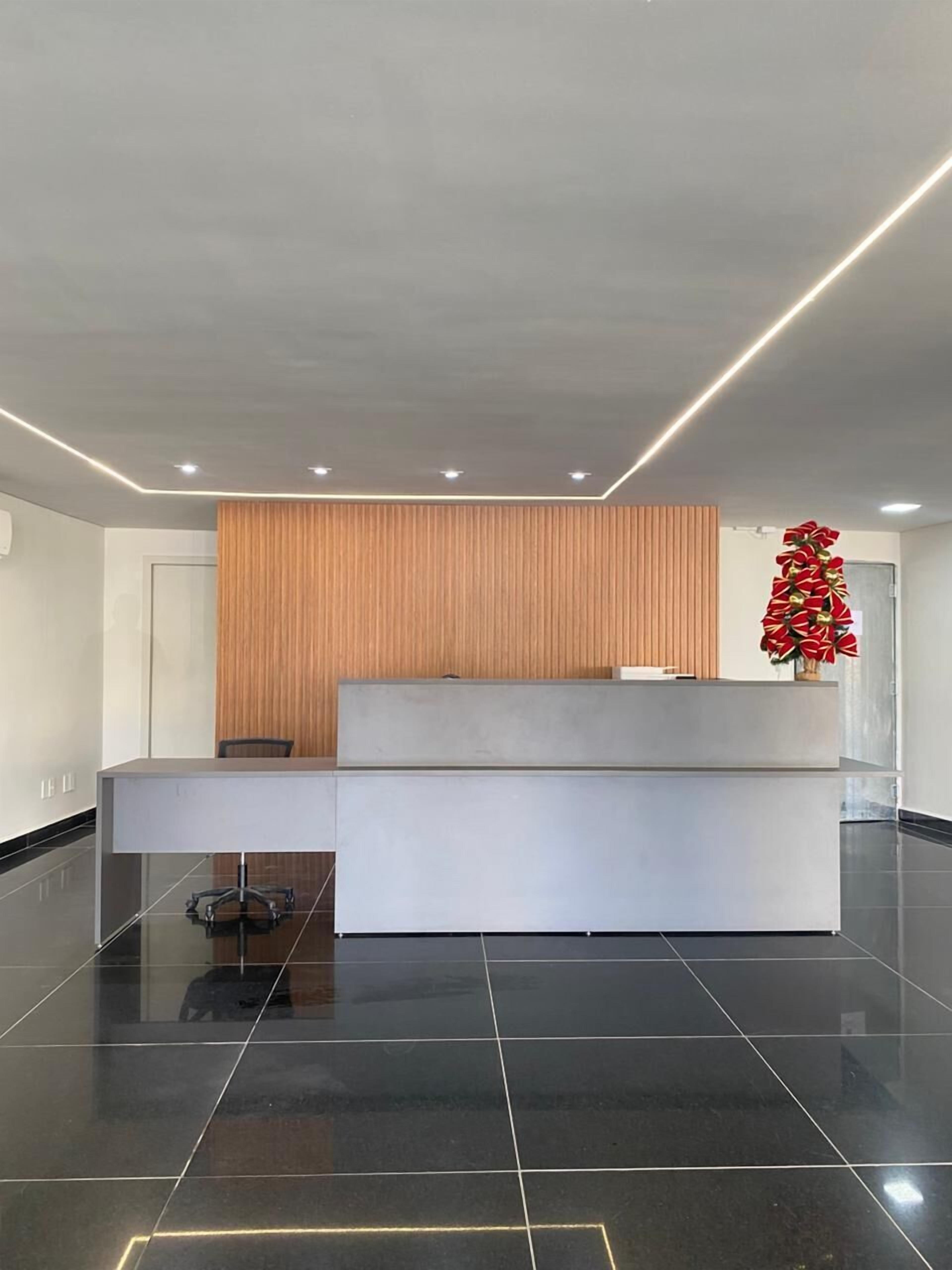 Un mostrador de recepci ón moderno con un panel de madera de fondo, una partición de vidrio y un arreglo floral decorativo rojo.