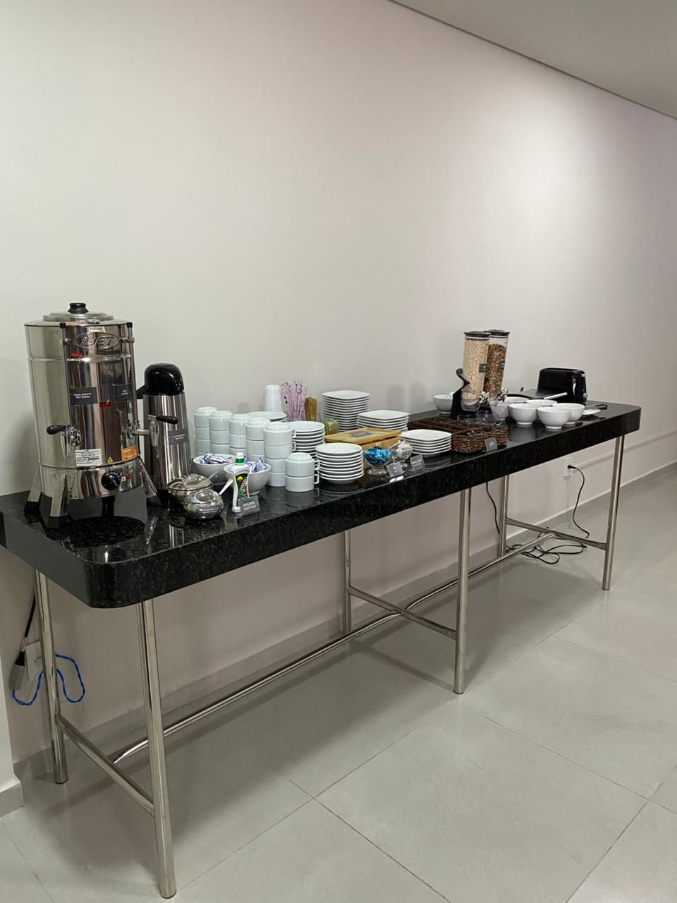 Un buffet allestito con una macchina per il caffè, piatti, tazze e un frullatore su un piano di lavoro nero.