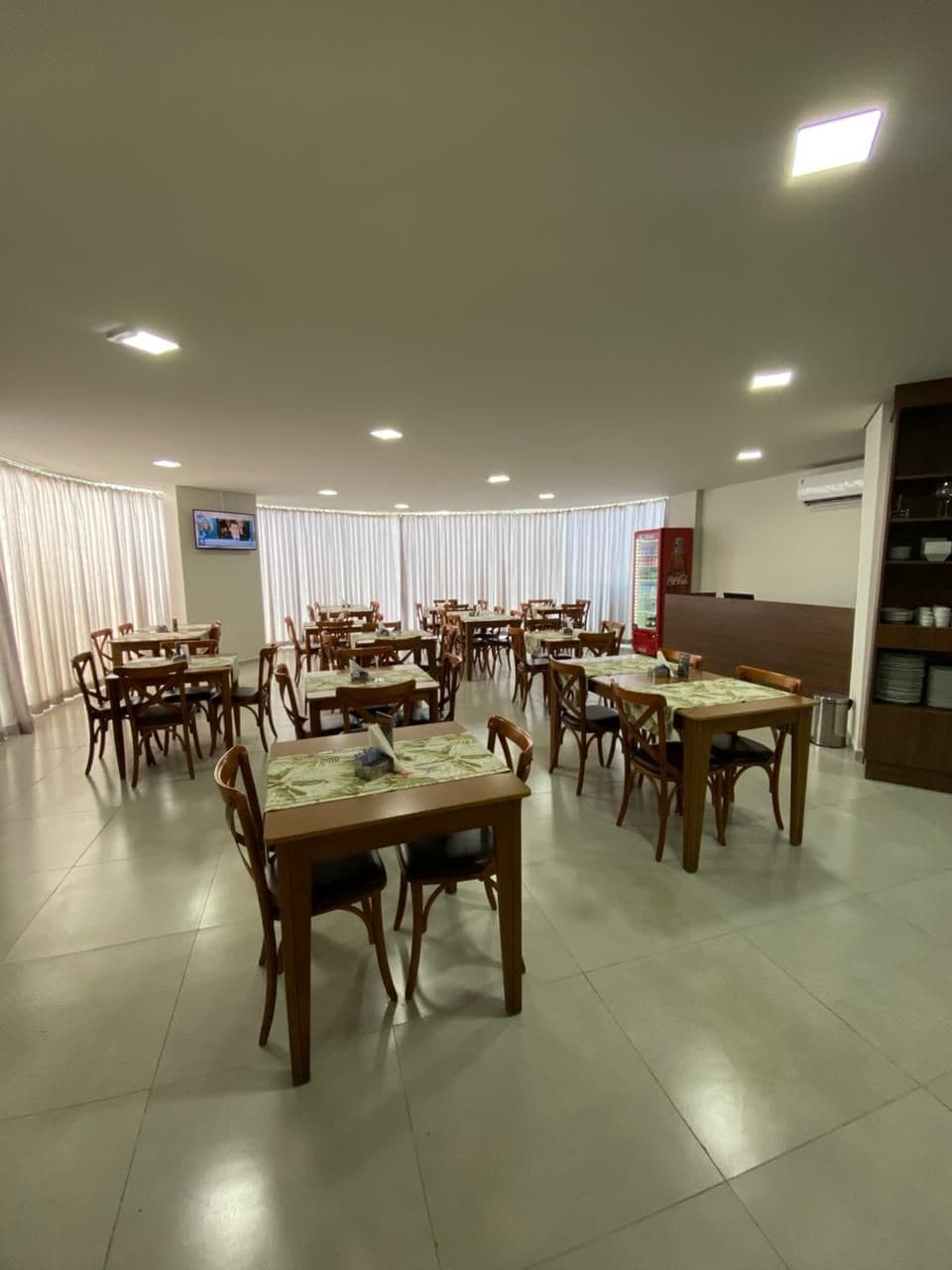 Un espace repas avec plusieurs tables et chaises, un distributeur automatique et un écran de télévision fixé au mur.
