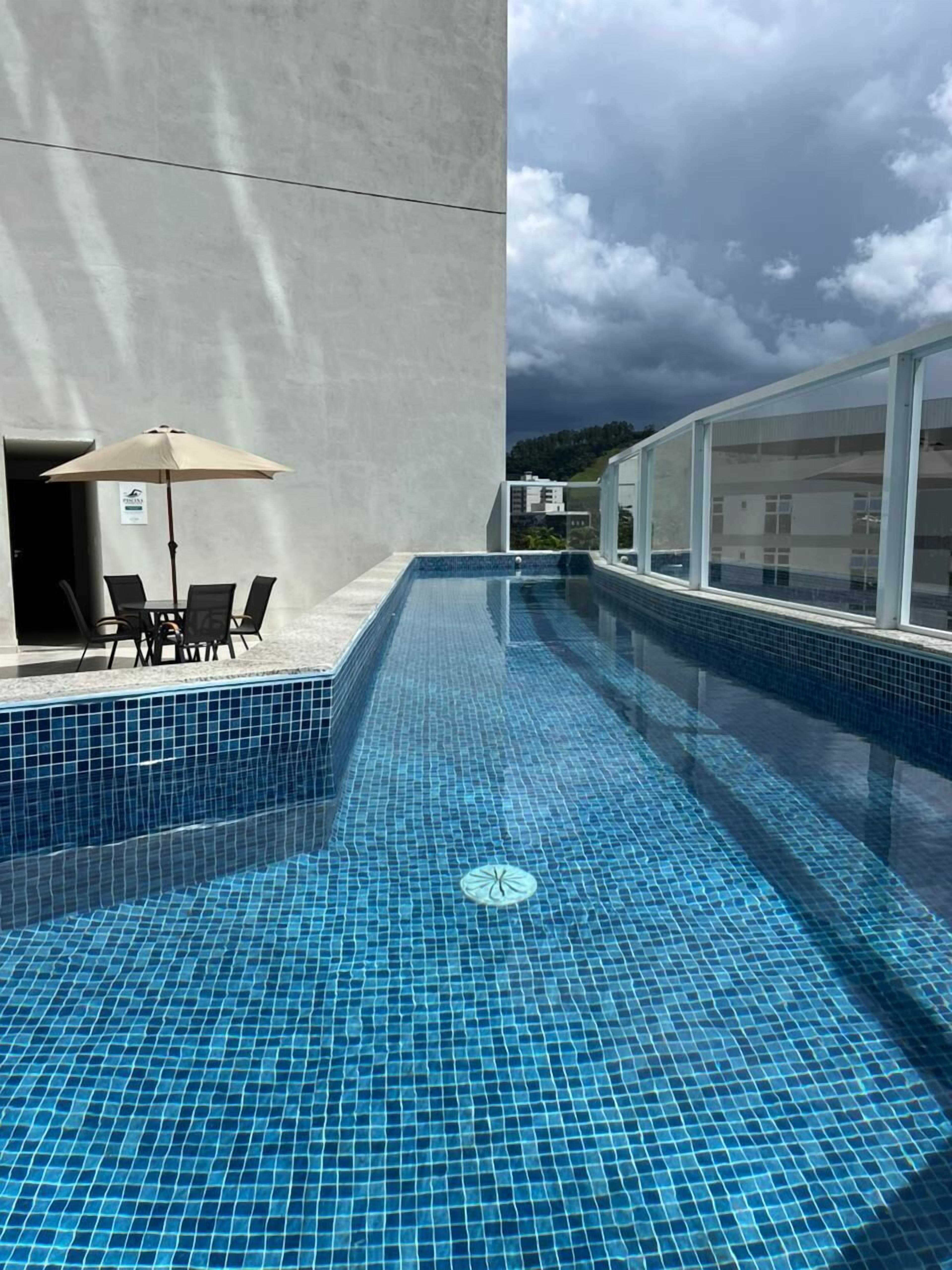 A swimming pool with blue tiles, a table with chairs, and a large umbrella.