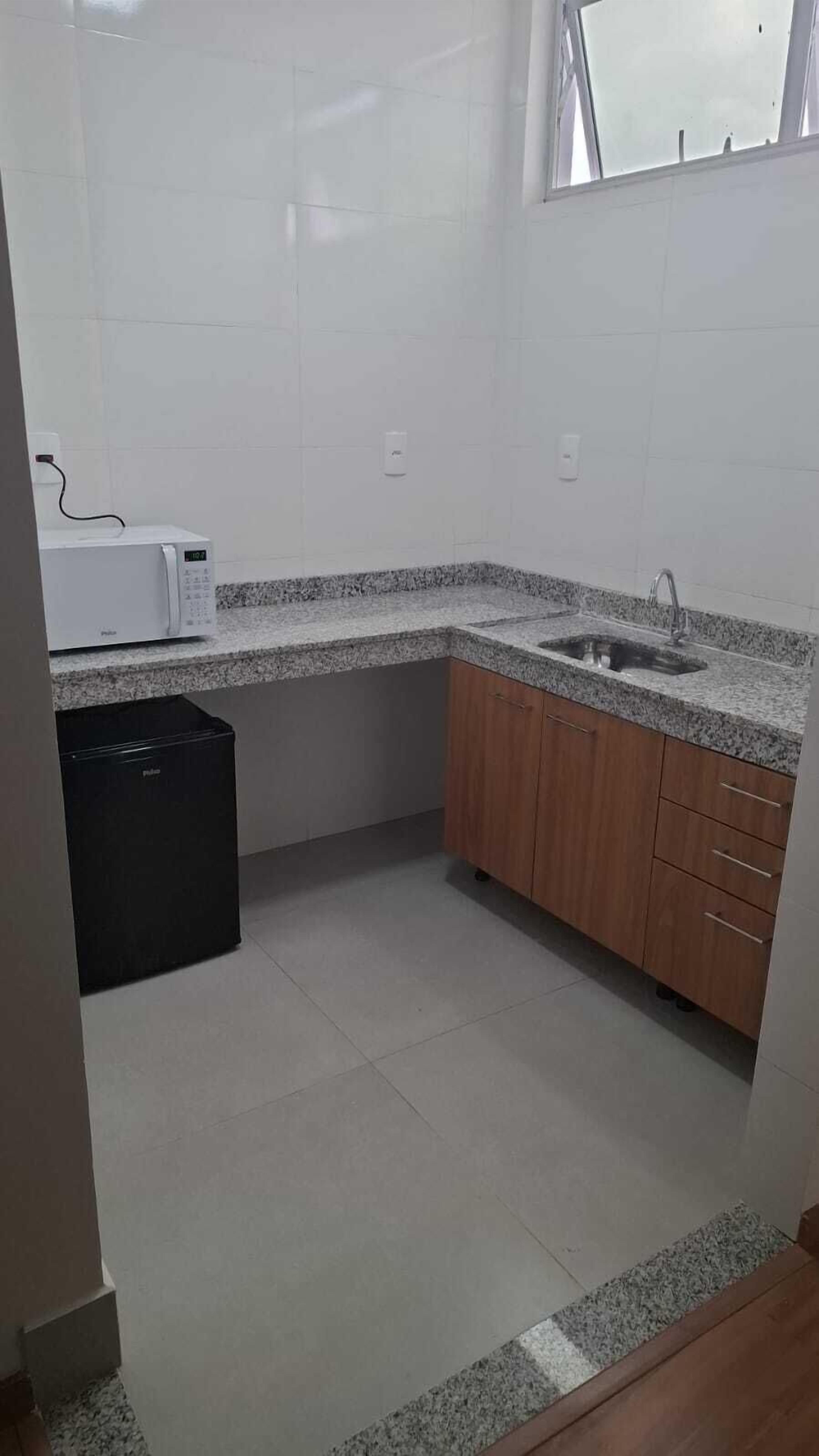 Uma cozinha pequena com azulejos brancos, micro-ondas, pia e armários de madeira.