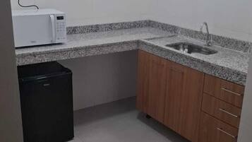Uma cozinha pequena com azulejos brancos, micro-ondas, pia e armários de madeira.