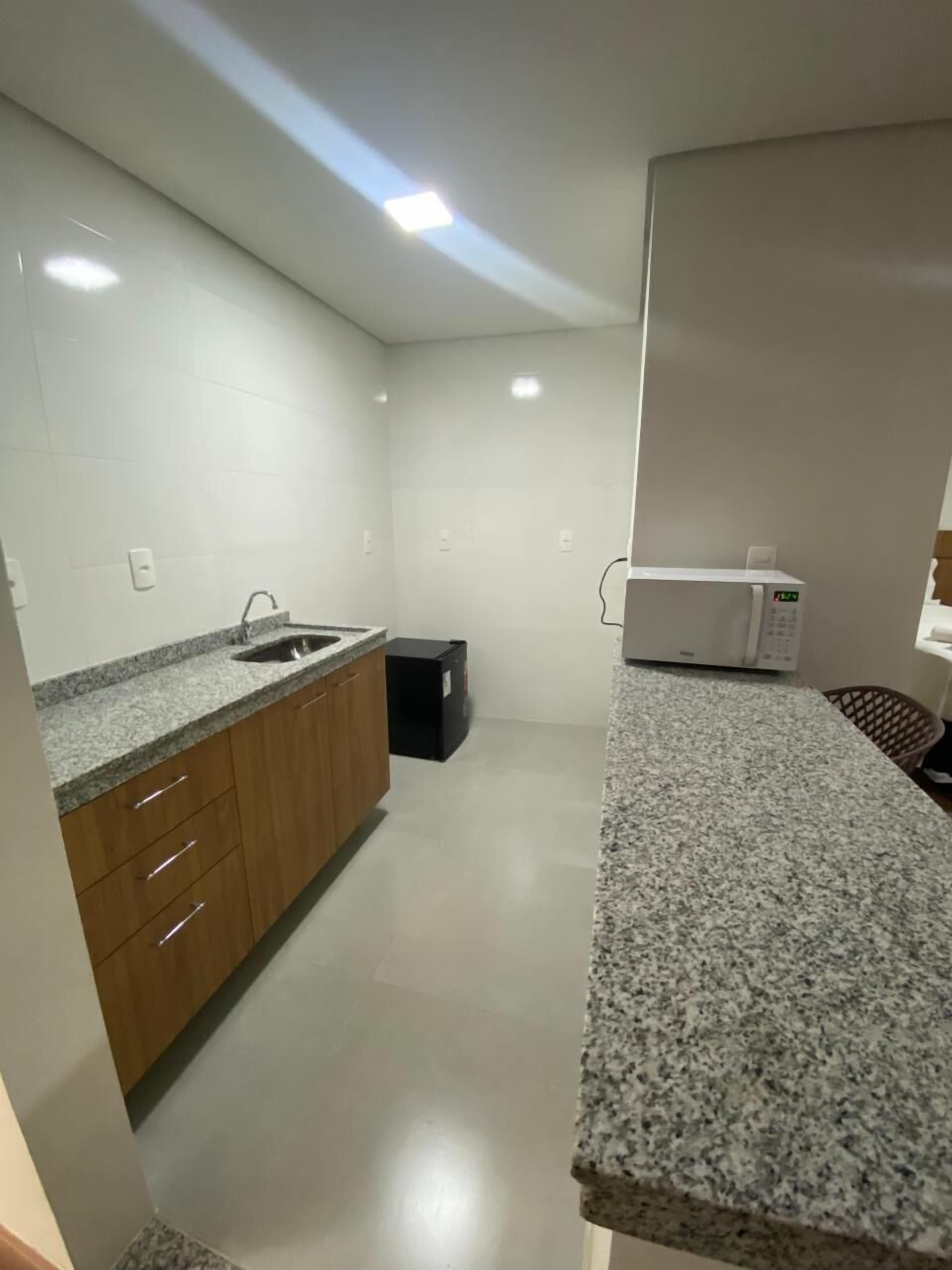 A modern kitchen with granite countertops, wooden cabinets, a black trash bin, and a white microwave.