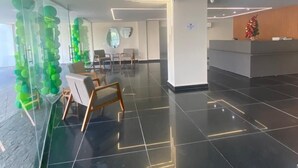 A modern lobby with a glass partition, a reception desk, and a seating area with chairs. - San Diego Suites Manhuaçu (Manhuaçu)