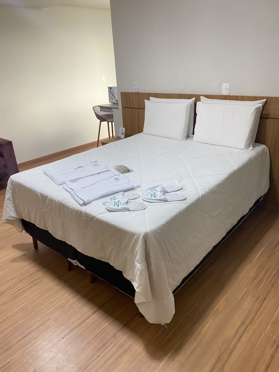 A neatly made bed with a white bedspread, pillows, and a set of white slippers and towels on the bed.