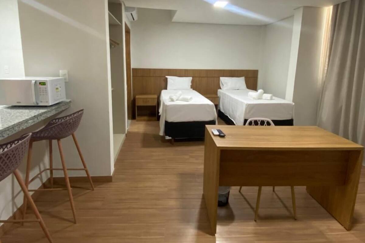 A hotel room with a wooden floor, a desk with a chair, two single beds, a small table, and a microwave on the counter.
