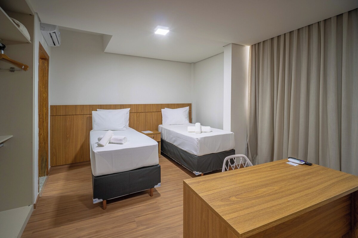 Habitación de hotel con dos camas, un escritorio de madera y una ventana con cortinas.