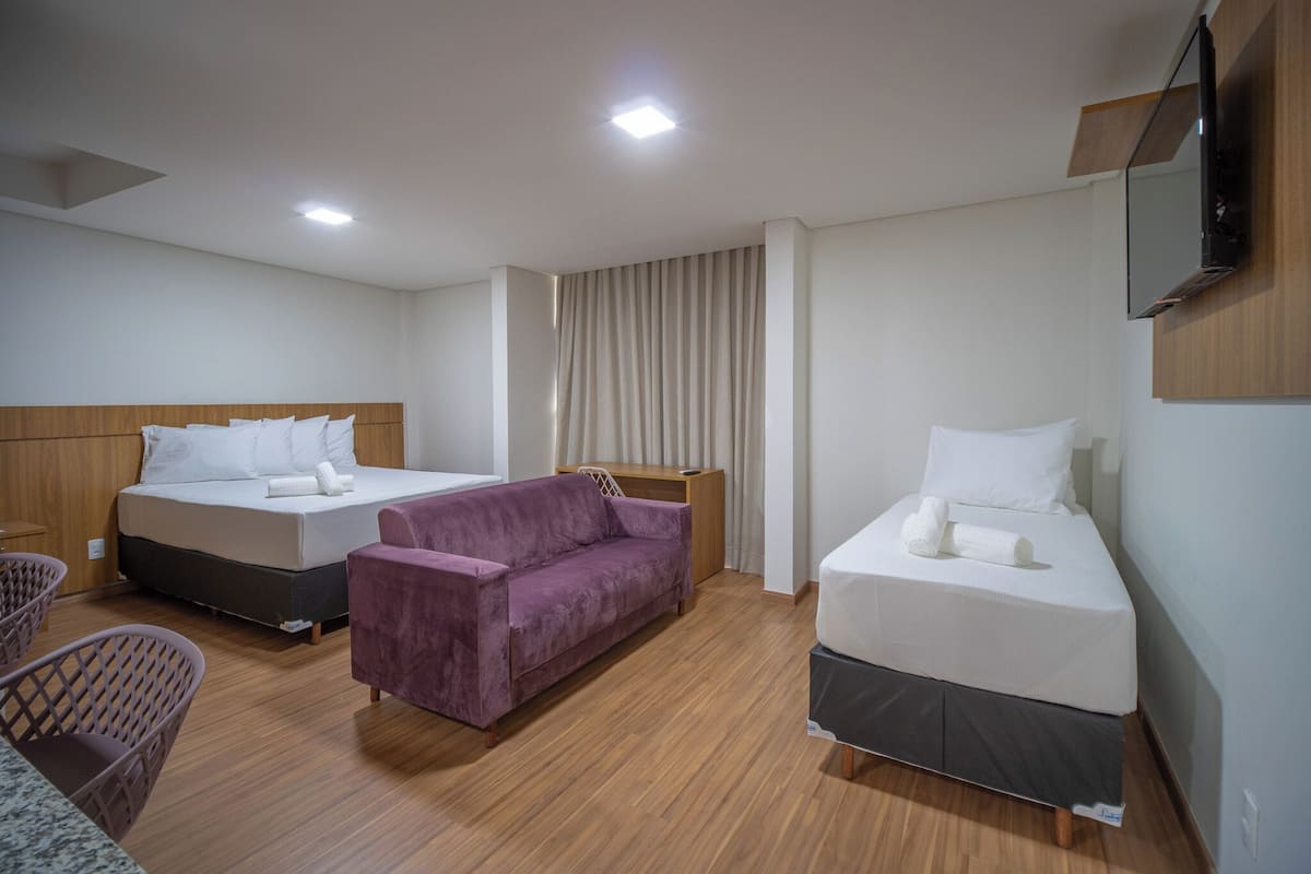 A hotel room with two beds, a purple sofa, and a TV mounted on the wall.