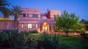 A modern building with a central archway, surrounded by lush gardens and palm trees. - Domaine 3 Riads  (Marrakech)