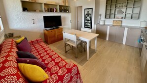 Un espacio habitable compacto con sofá, televisor, mesa de comedor y kitchenette.