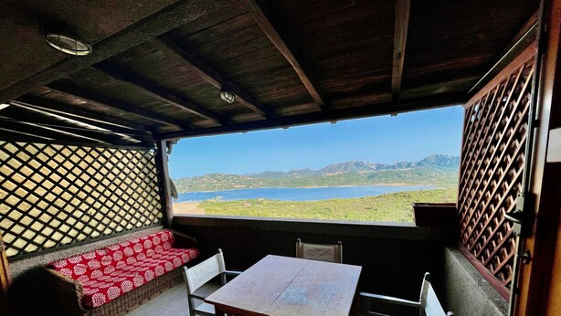 Una habitación con techo de madera, una mesa con sillas, un sofá estampado y vistas a un lago y montañas.