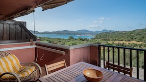 A balcony with a wooden table, a wicker chair, and a view of a coastal landscape. - Rena Bianca House by Wonderful Italy (Olbia)