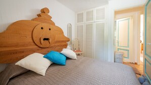 Ein Schlafzimmer mit hölzernem Kopfteil, einem Bett mit gesteppter Bettdecke und einem Korbstuhl.